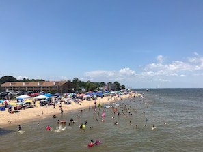 A beach with people swimming and sunbathing, umbrellas, and a hotel in the background.