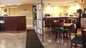 Vestíbulo de hotel con una recepción, un área de descanso con mesas y sillas, un refrigerador y un reloj en la pared.
