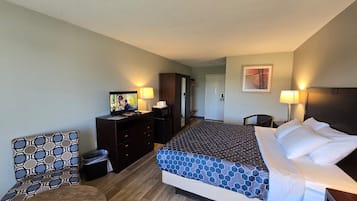 A hotel room with a bed, a desk with a television, a chair, and a door leading to another room.