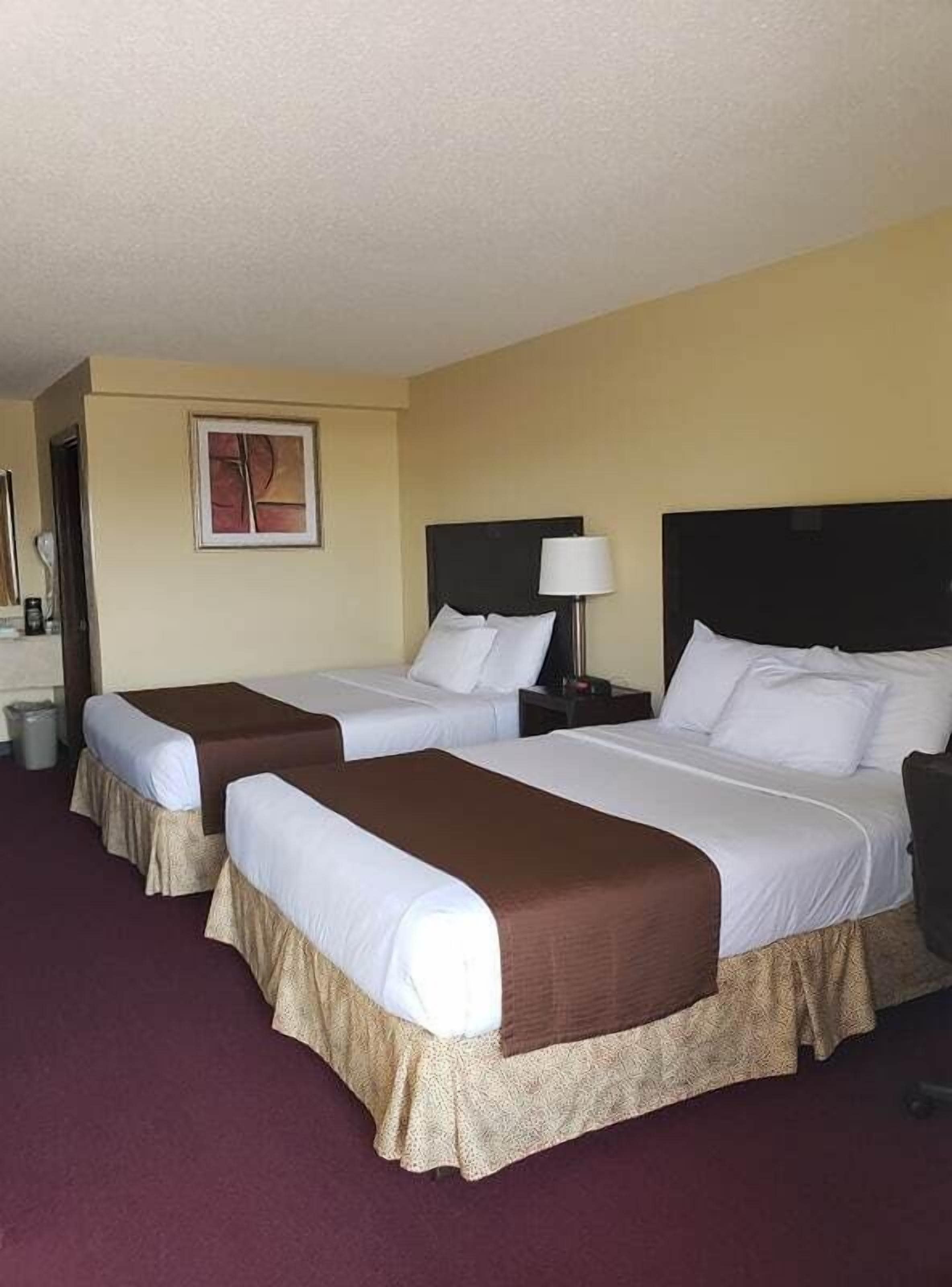 A hotel room with two beds, a nightstand with a lamp, and a painting on the wall.