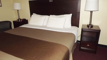 A hotel room with a large bed, two bedside tables with lamps, a chair, and a carpeted floor.