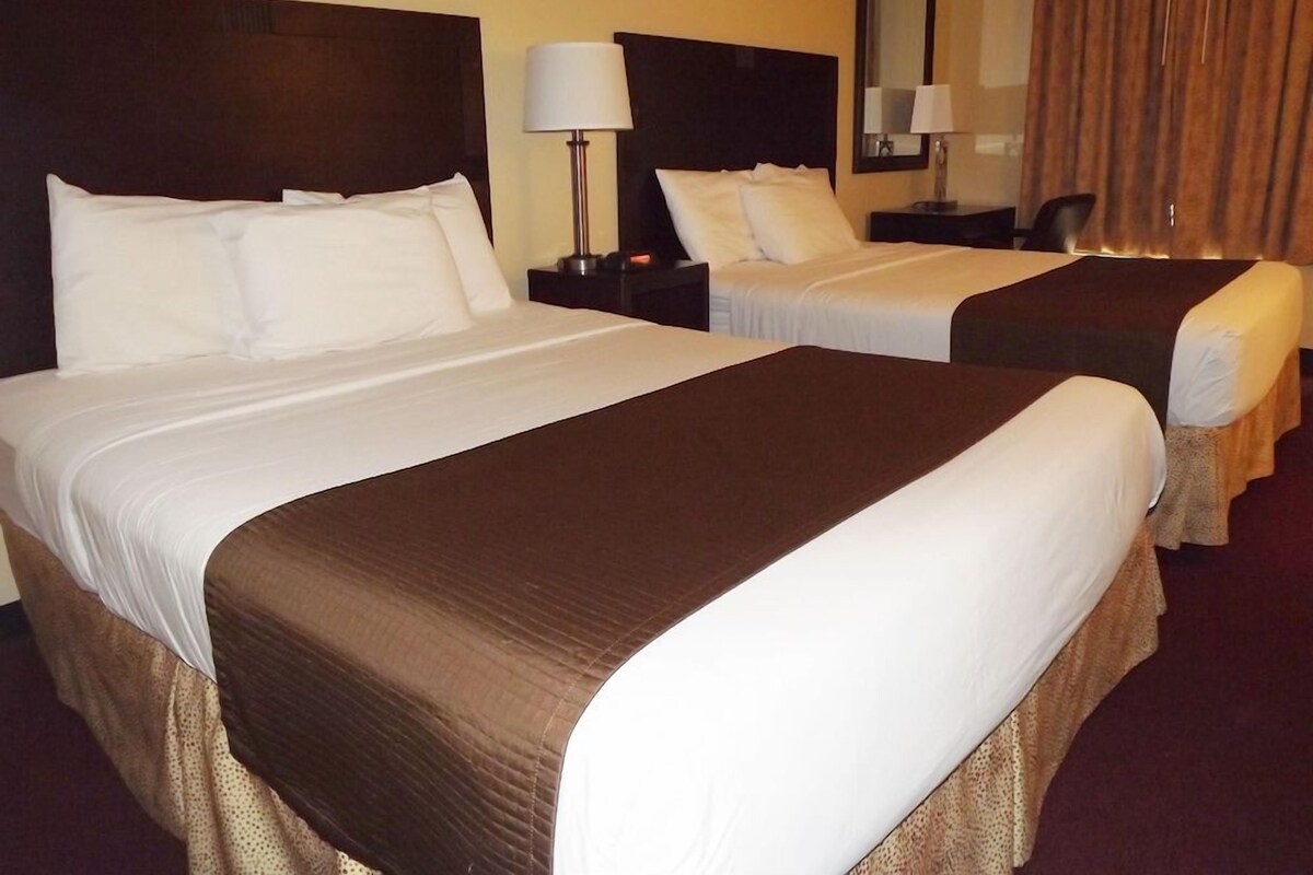 Habitación de hotel con dos camas, una mesita de noche con lámpara, una silla y un espejo en la pared.