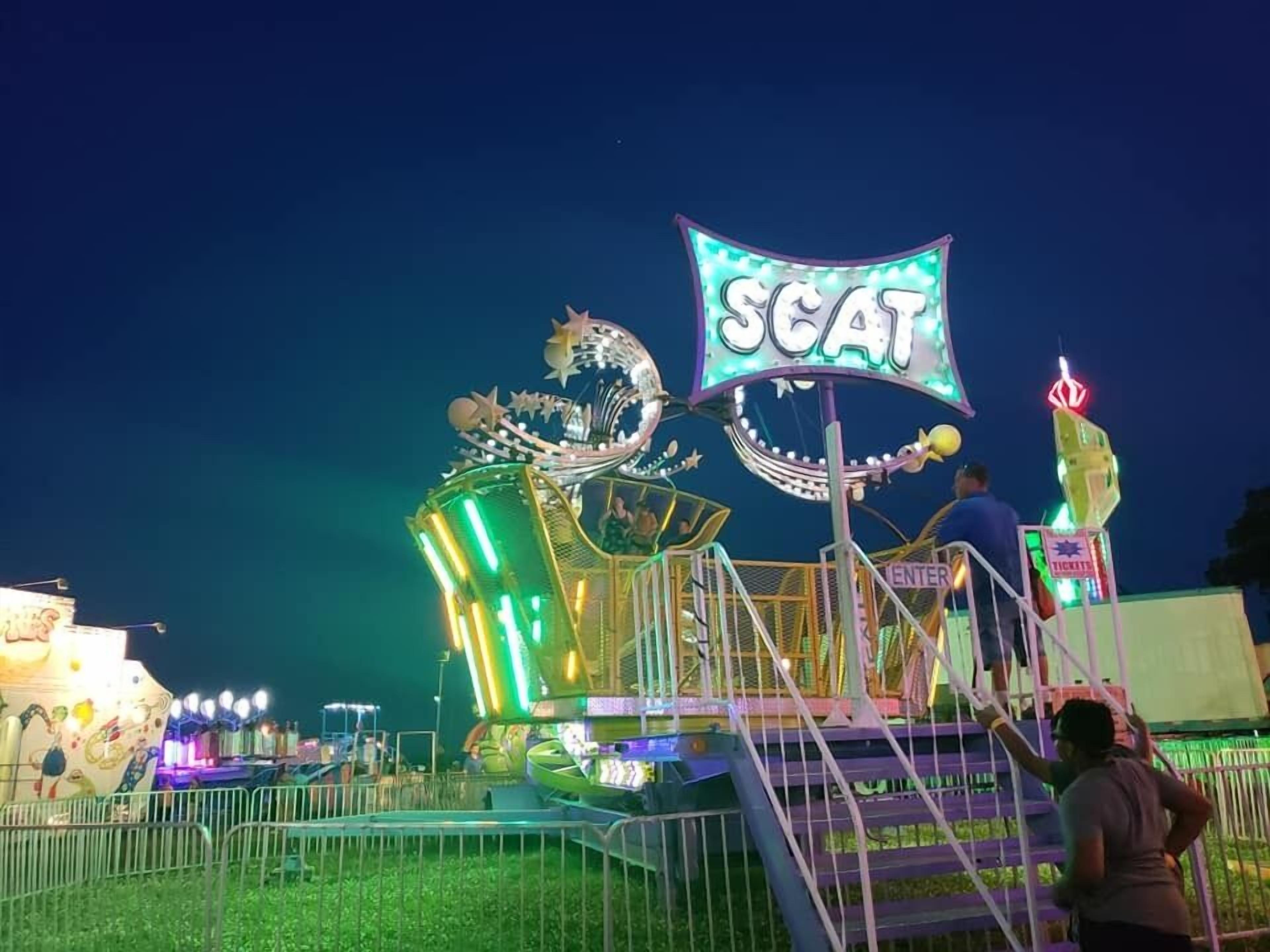 A brightly lit amusement ride with a sign that reads "SCAT" and a ticket booth nearby.