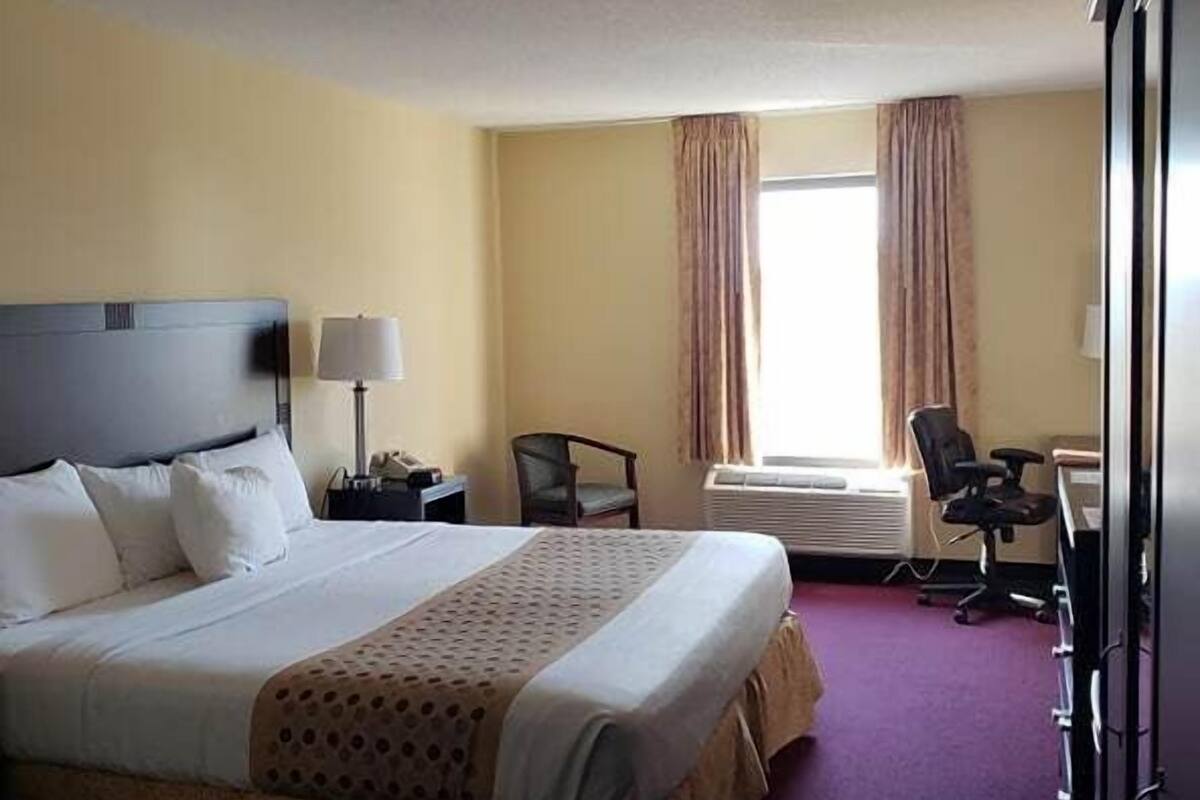 A hotel room with a large bed, a desk, a chair, and a window with curtains.