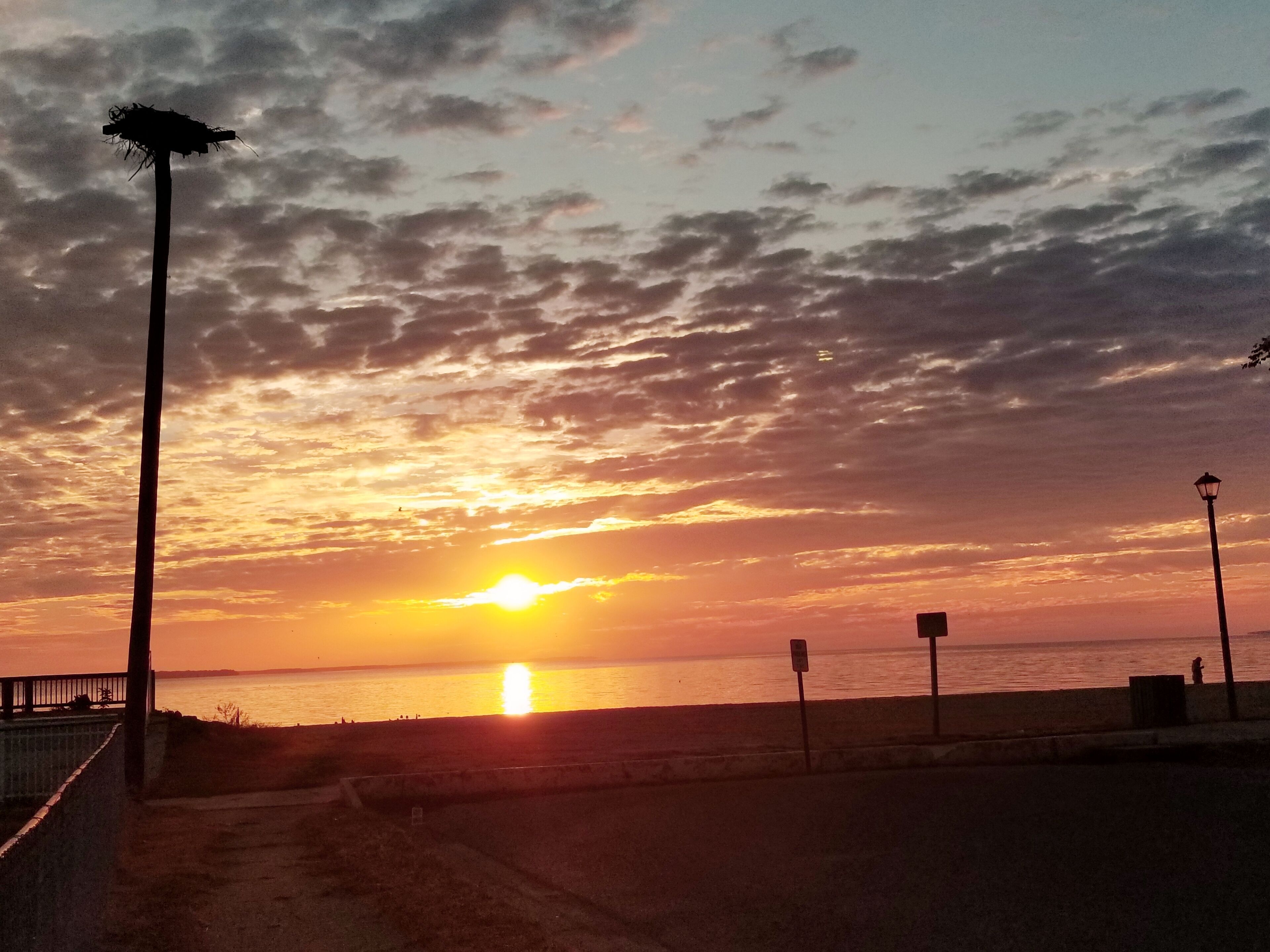 A sunset over a beach with a fence and street lamps.