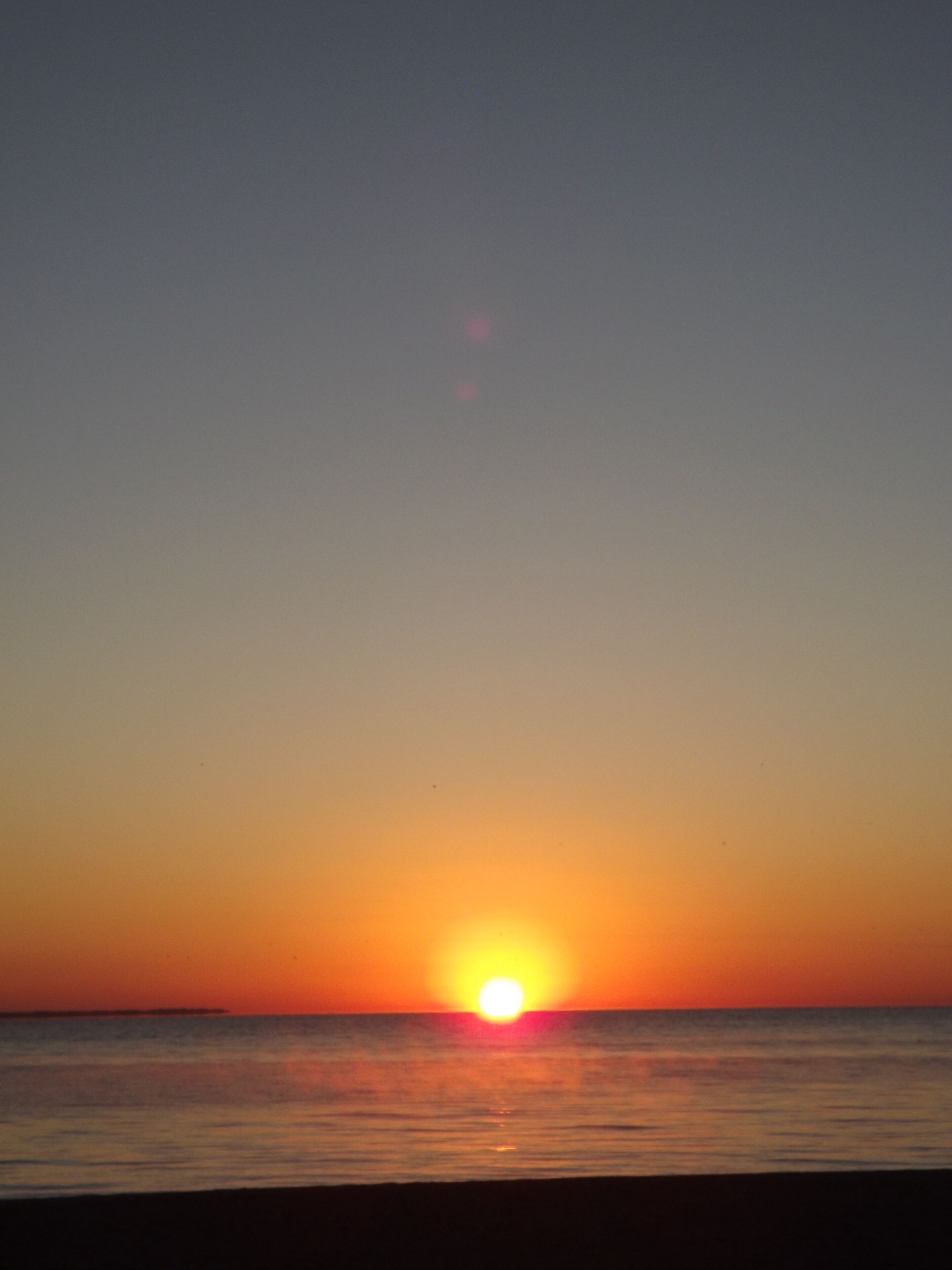 Un atardecer sobre un mar tranquilo con un horizonte despejado.