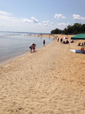 A sandy beach with people, umbrellas, and a green tent. - River Edge Inn (Colonial Beach)