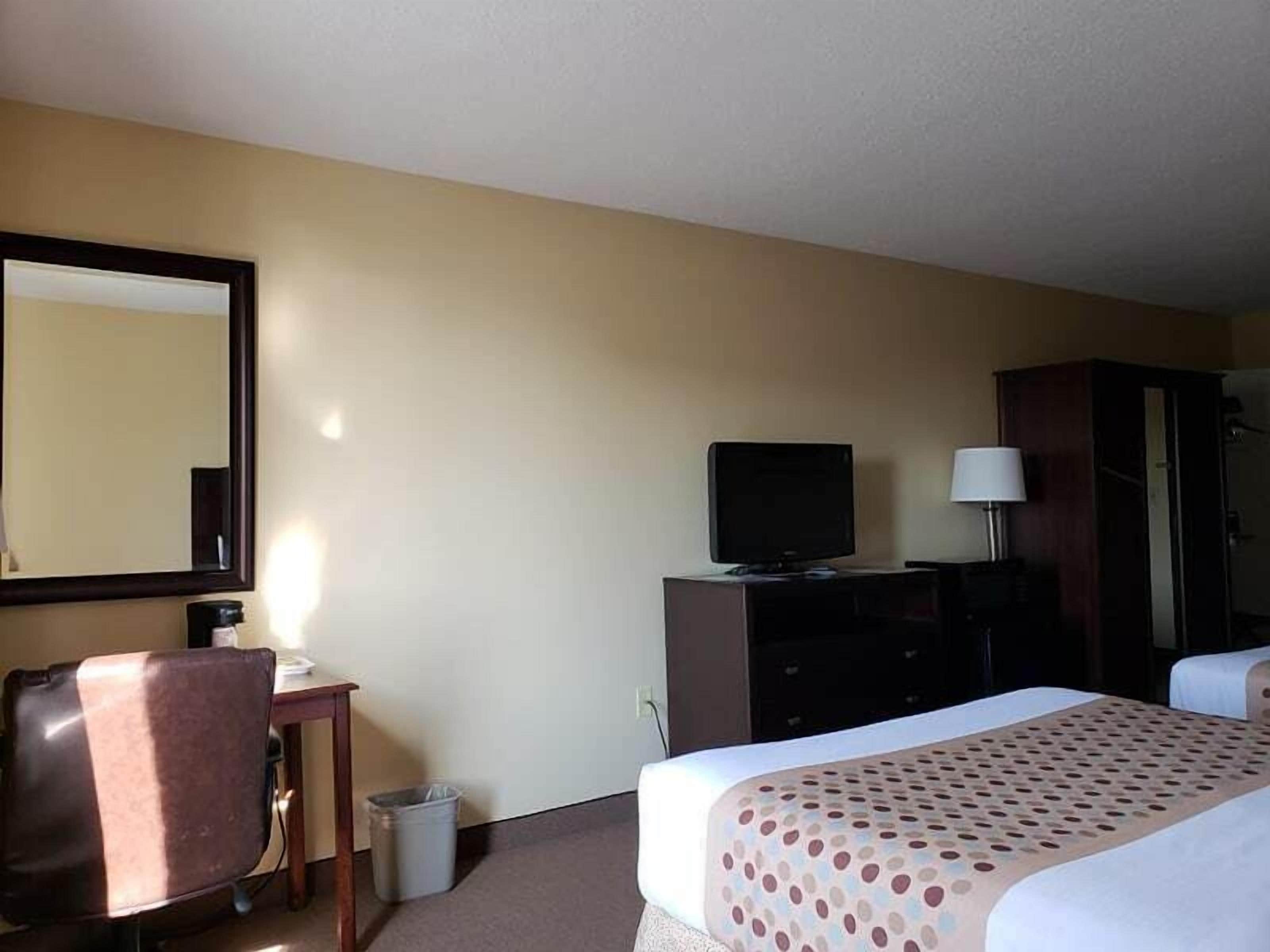 A hotel room with a bed, a desk, a television, a mirror, and a wardrobe.