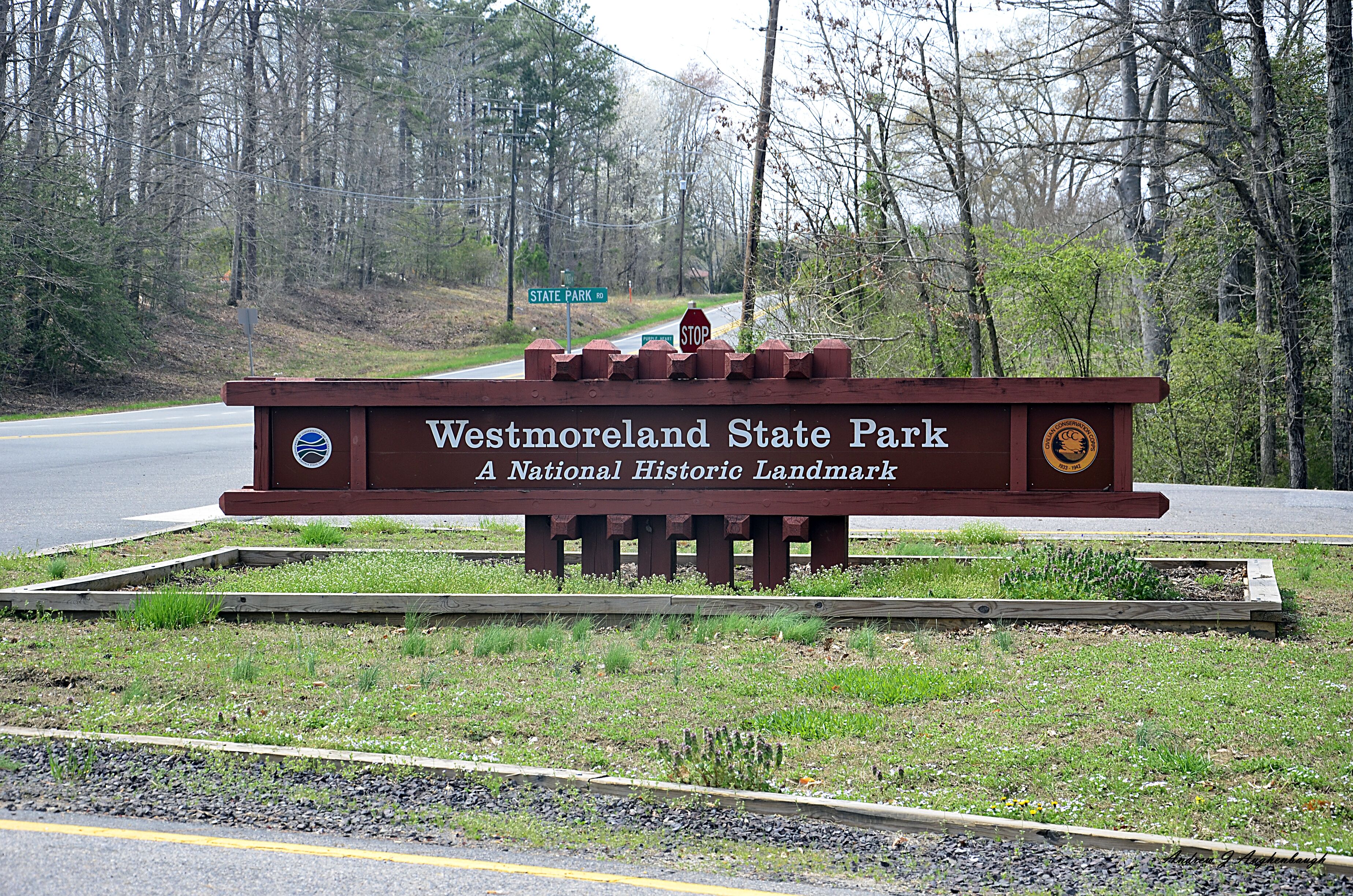 A sign for Westmoreland State Park, a National Historic Landmark, with a stop sign and a road in the background.