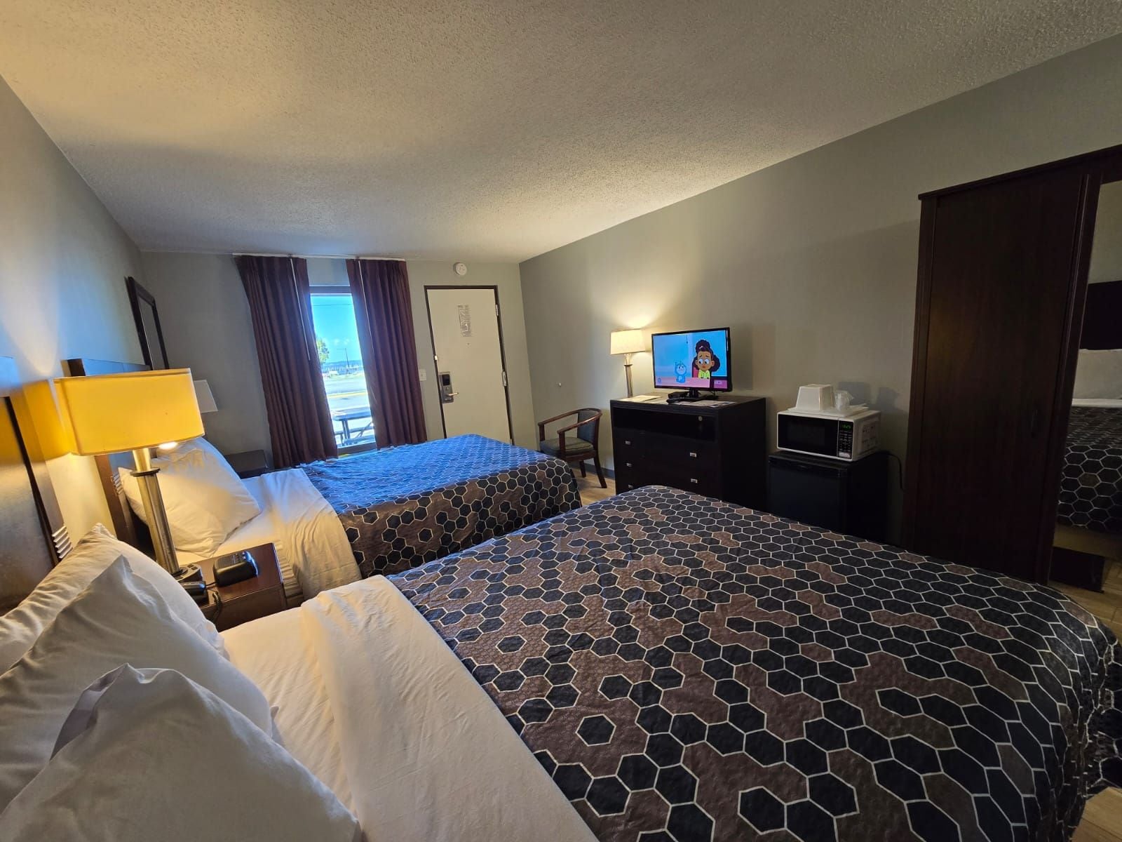 A hotel room with two beds, a television, a desk, and a view of the outdoors.