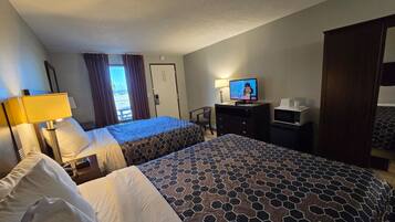 A hotel room with two beds, a television, a desk, and a view of the outdoors.