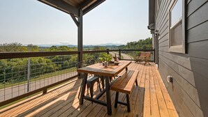 A wooden deck with a table and benches, overlooking a scenic landscape with trees and mountains. - Modern Cabin with Private Pool (Sevierville)