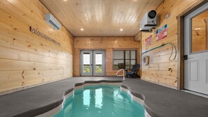 A swimming pool with wooden walls and a ceiling, a lifeguard chair, and a door with a window. - Modern Cabin with Private Pool (Sevierville)