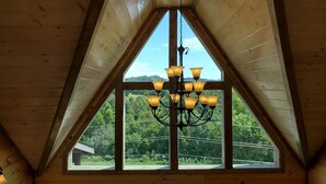 A room with a wooden ceiling, a chandelier, and large windows offering a view of greenery. - Modern Cabin with Private Pool (Sevierville)