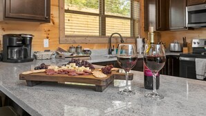 A kitchen counter with a charcuterie board, wine glass, and a bottle of wine. - Modern Cabin with Private Pool (Sevierville)