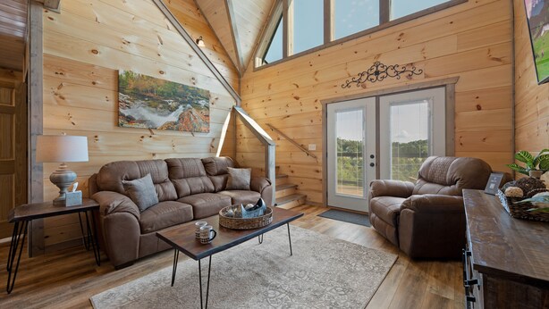 A cozy wooden cabin interior with a sofa, a coffee table, and a dining table. - Modern Cabin with Private Pool (Sevierville)