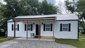 A small, single-story building with a covered porch and a gravel driveway. - Edina Missouri New Cabin in Rural Area (Edina)