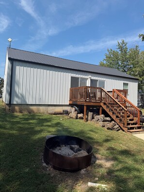A metal building with a wooden deck and stairs, a fire pit, and logs in the yard. - Edina Missouri New Cabin in Rural Area (Edina)