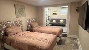 A bedroom with two beds, a TV, and a hallway leading to a living area. - ArtSea 1 · 2BR at LECOM, Beaches, Ample Parking -Downtown (Bradenton)