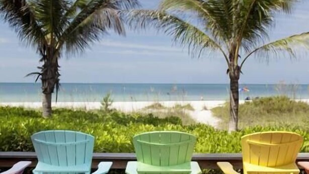 Three Adirondack chairs facing a beach with palm trees and ocean views. - ArtSea 1 · 2BR at LECOM, Beaches, Ample Parking -Downtown (Bradenton)