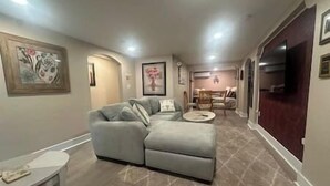 A modern living room with a sectional sofa, a round coffee table, and a dining area in the background. - ArtSea 1 · 2BR at LECOM, Beaches, Ample Parking -Downtown (Bradenton)