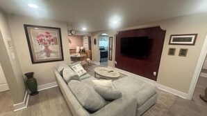 A living room with a grey sectional sofa, a coffee table, and a flat-screen TV mounted on the wall. - ArtSea 1 · 2BR at LECOM, Beaches, Ample Parking -Downtown (Bradenton)