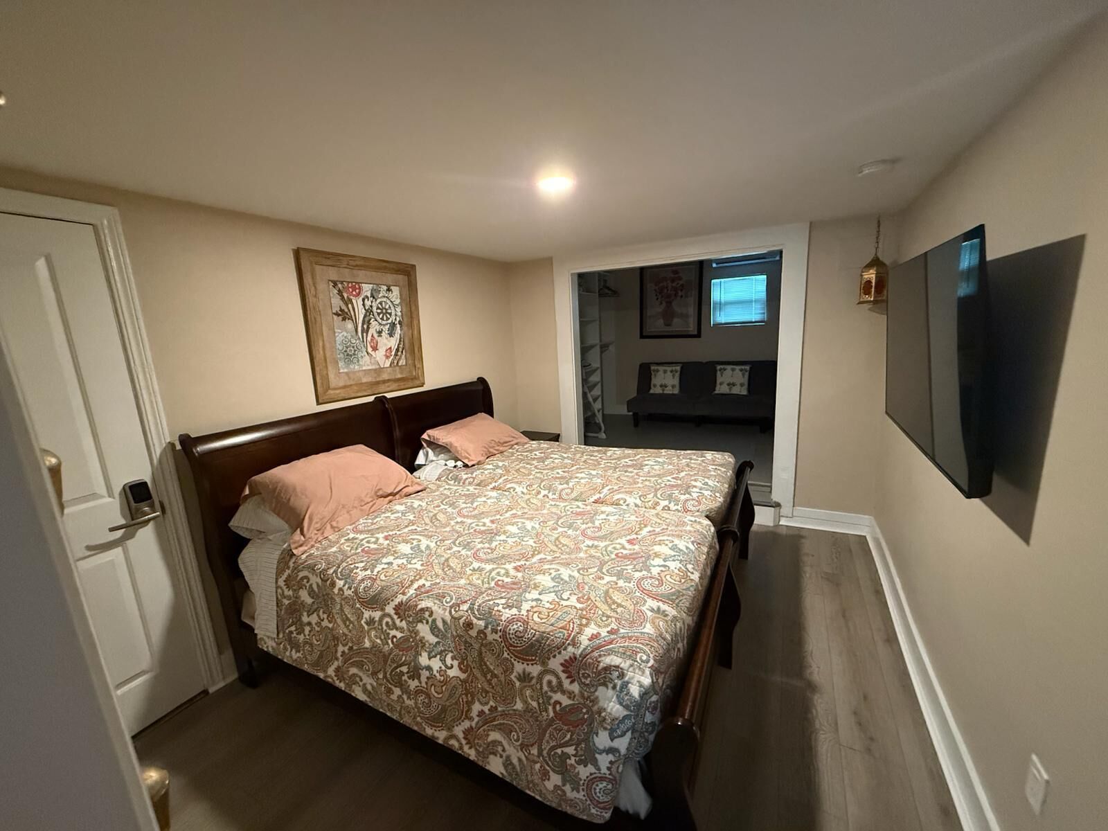A bedroom with a bed, a door, a hallway, a sofa, and a TV.