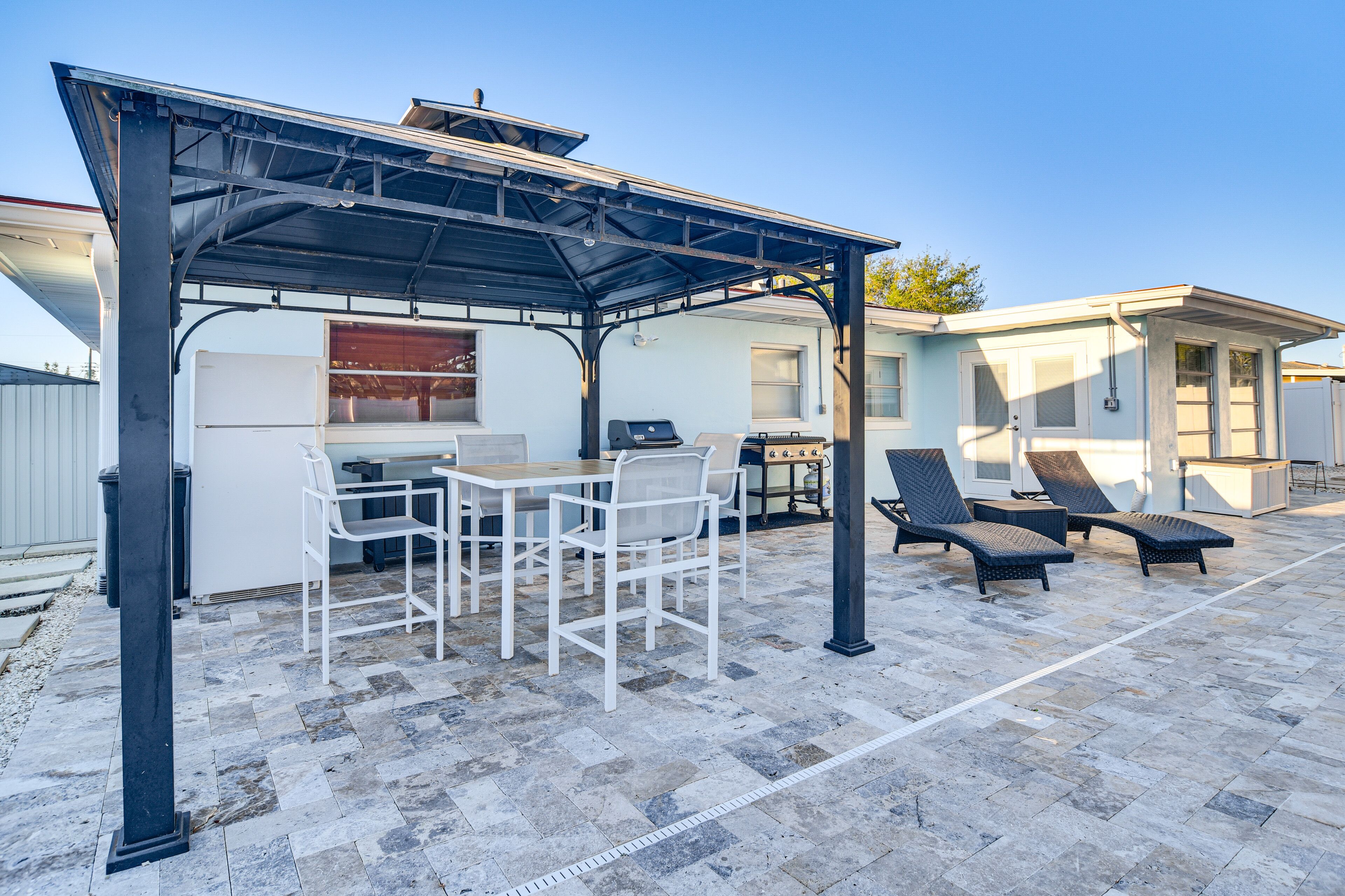 An outdoor patio with a covered grill area, white furniture, and lounge chairs.