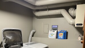 Ein Waschraum mit einer Frontlader-Waschmaschine und einem Trockner, einer Fantech-Heizung und zwei Waschmittelflaschen an der Wand.