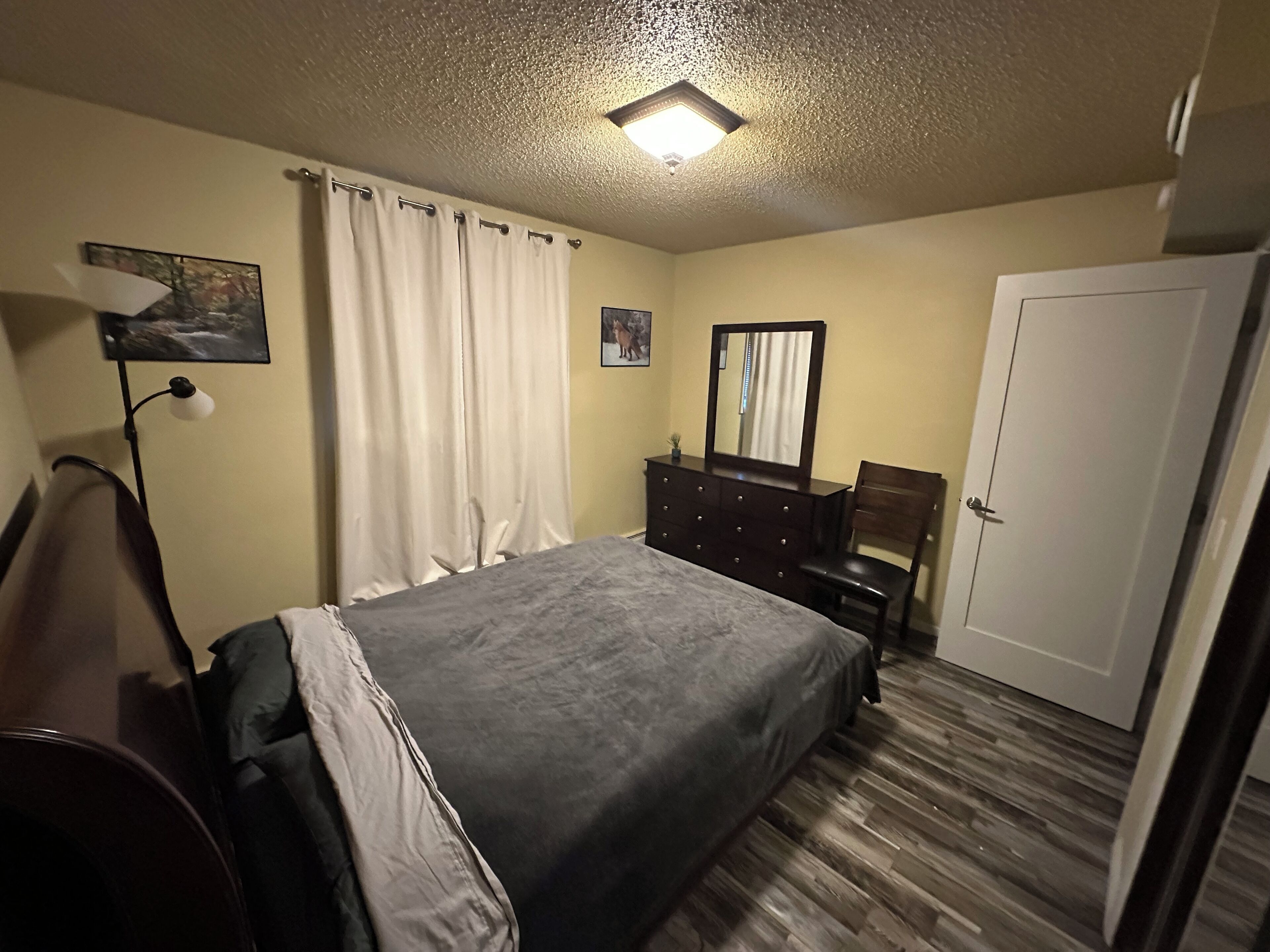 Un dormitorio con cama, cómoda, silla, escritorio, lámpara y puerta.