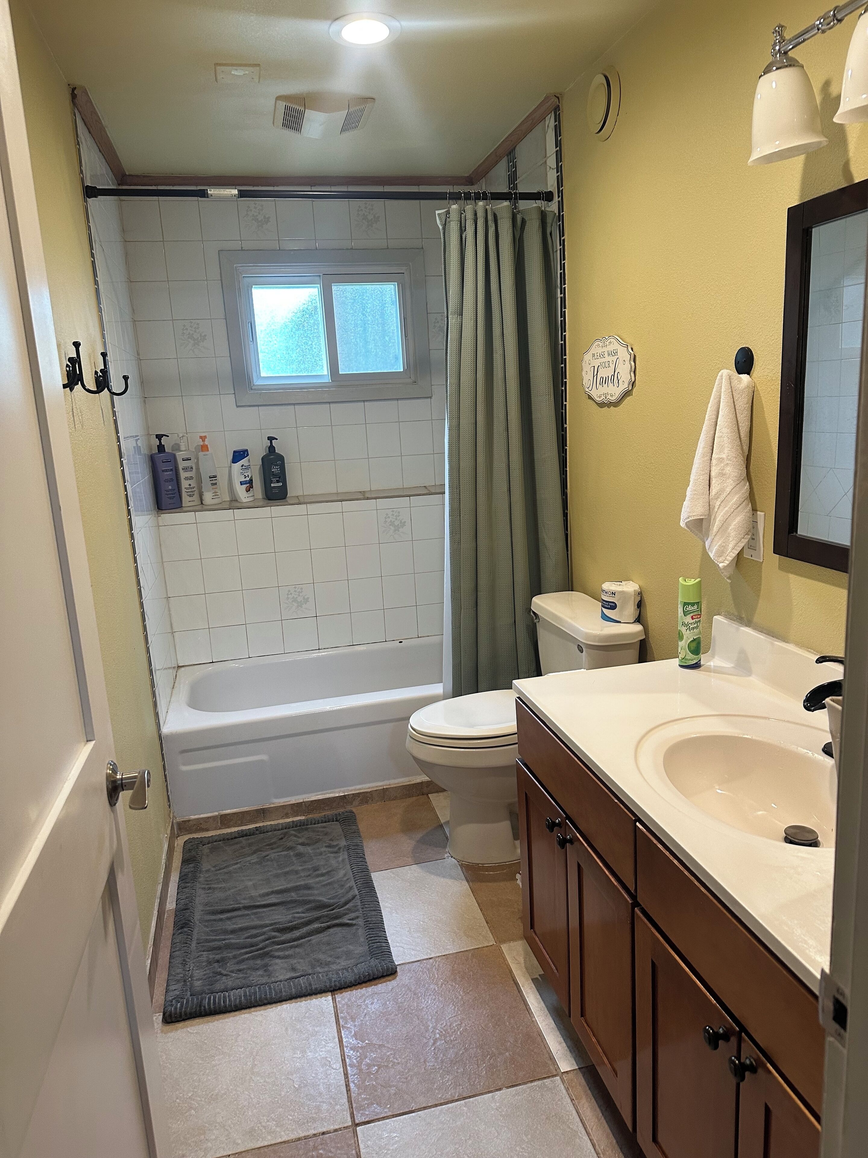 Une salle de bain avec une baignoire, des toilettes et un lavabo. Il y a une fenêtre au-dessus de la baignoire, une serviette accrochée au mur et un rideau de douche.