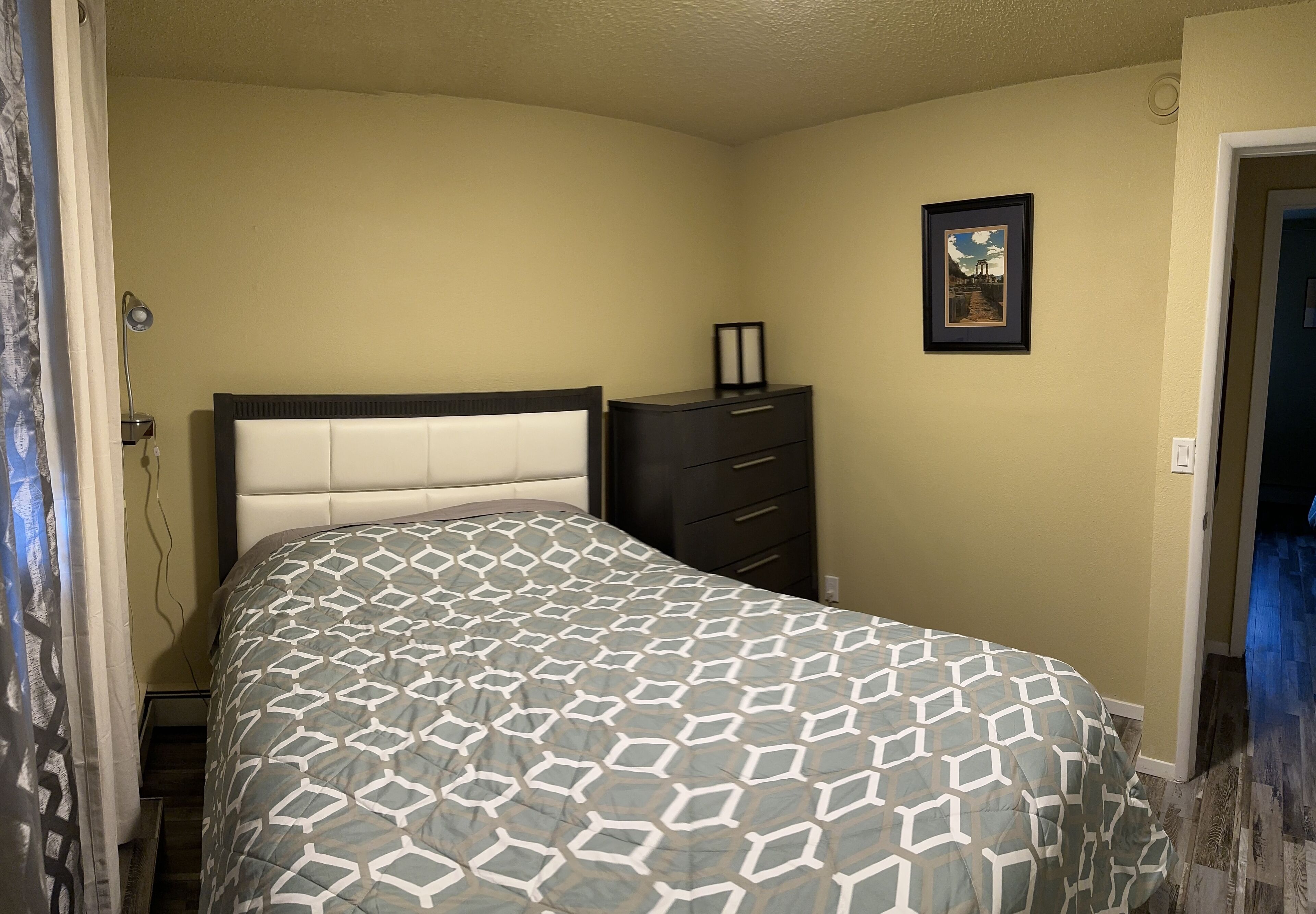 A bedroom with a bed, a dresser, and a framed picture on the wall.