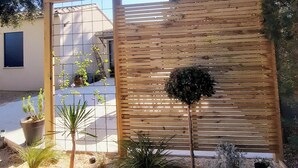 Una cerca de madera con diseño de cuadrícula, rodeada de diferentes plantas en macetas y un pequeño árbol.