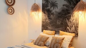 Un dormitorio con una cama, dos adornos circulares en la pared, un gran mural tropical y dos lámparas colgantes.