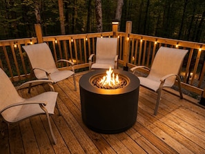 A deck with a circular fire pit surrounded by four chairs. - Spacious Treetop Cabin Perfect for Large Families! (Bellaire)