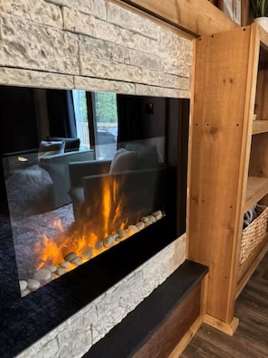 A modern fireplace with a stone facade, a black hearth, and a visible fire. - Spacious Treetop Cabin Perfect for Large Families! (Bellaire)