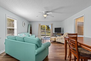Ein Wohnzimmer mit einem türkisfarbenen Sofa, einem Holzesstisch und einem Deckenventilator.