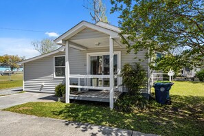 Einbungalow mit Veranda, kleinem Vorgarten und Mülltonne.
