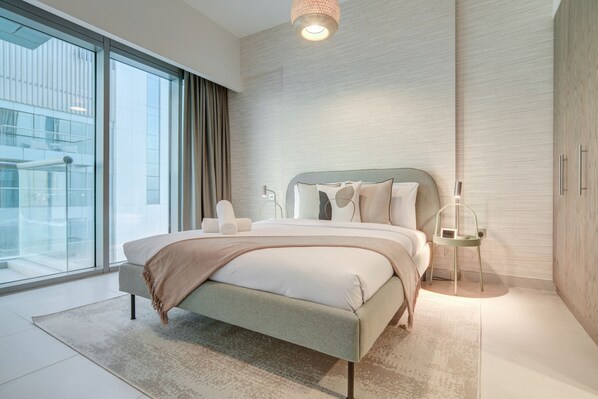 Une chambre moderne avec un grand lit, un mur en verre et une vue sur un immeuble.