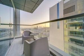Un balcon moderne offrant une vue sur la ville, doté d’une rambarde en verre et de mobilier contemporain.