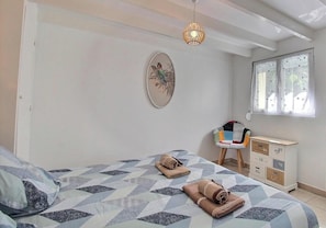 Un dormitorio con cama, una silla, un aparador, una ventana y una obra de arte colgada en la pared.