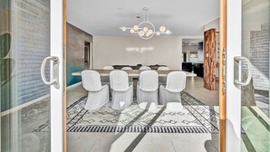 A modern dining area with a long table, six chairs, and a chandelier. - The Desert Trailhead Retreat Phoenix with Pool (Phoenix)