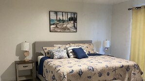 Een slaapkamer met een bed, nachtkastjes, een plafondventilator, een schilderij en een raam met gordijnen.