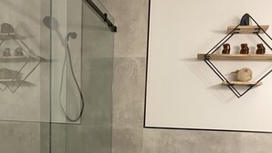Een moderne badkamer met een douchecabine van glas, een toilet en een plank met toiletartikelen.