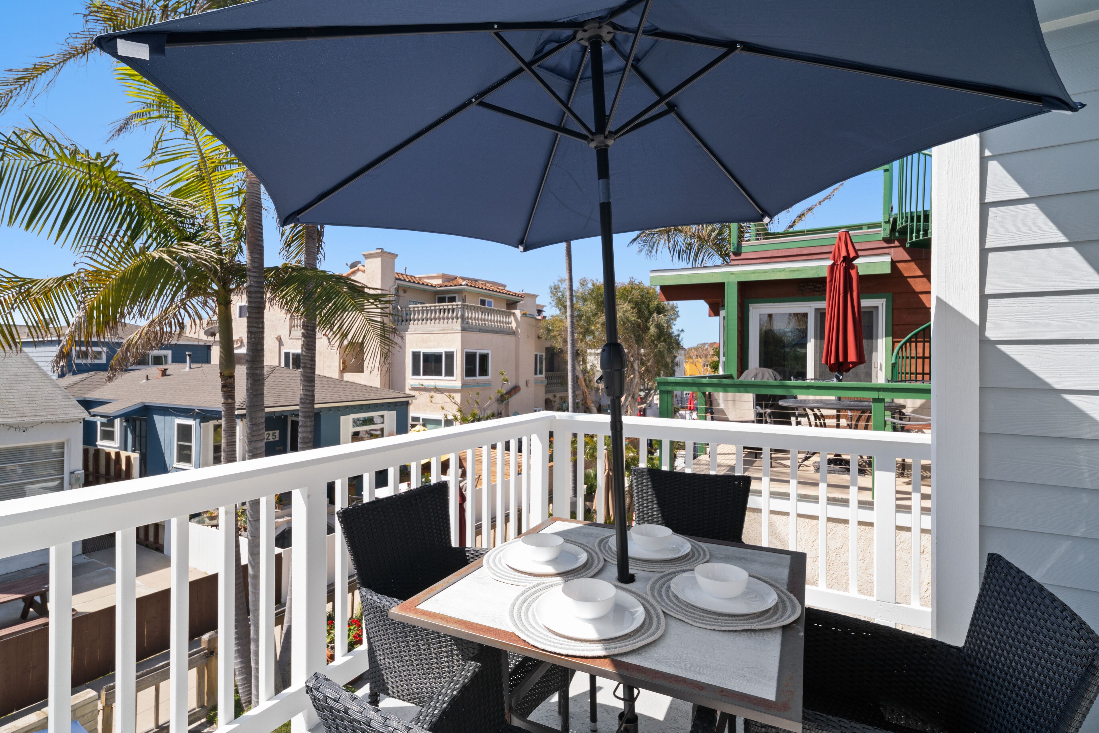A balcony with a table set for four, surrounded by white railings and wicker chairs.