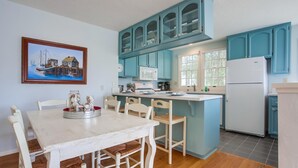 A kitchen with a white table, teal cabinets, and a painting of a harbor scene. - Spacious Family Beach Getaway | Scenic Bay Views, AC and Parking! (San Diego)