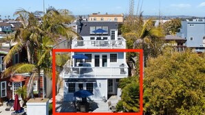 A two-story house with a balcony, surrounded by palm trees and other vegetation. - Spacious Family Beach Getaway | Scenic Bay Views, AC and Parking! (San Diego)