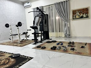 A home gym with exercise equipment, a patterned rug, and a painting on the wall. - Ibom Waterfall Resorts and Suites (Arochukwu)
