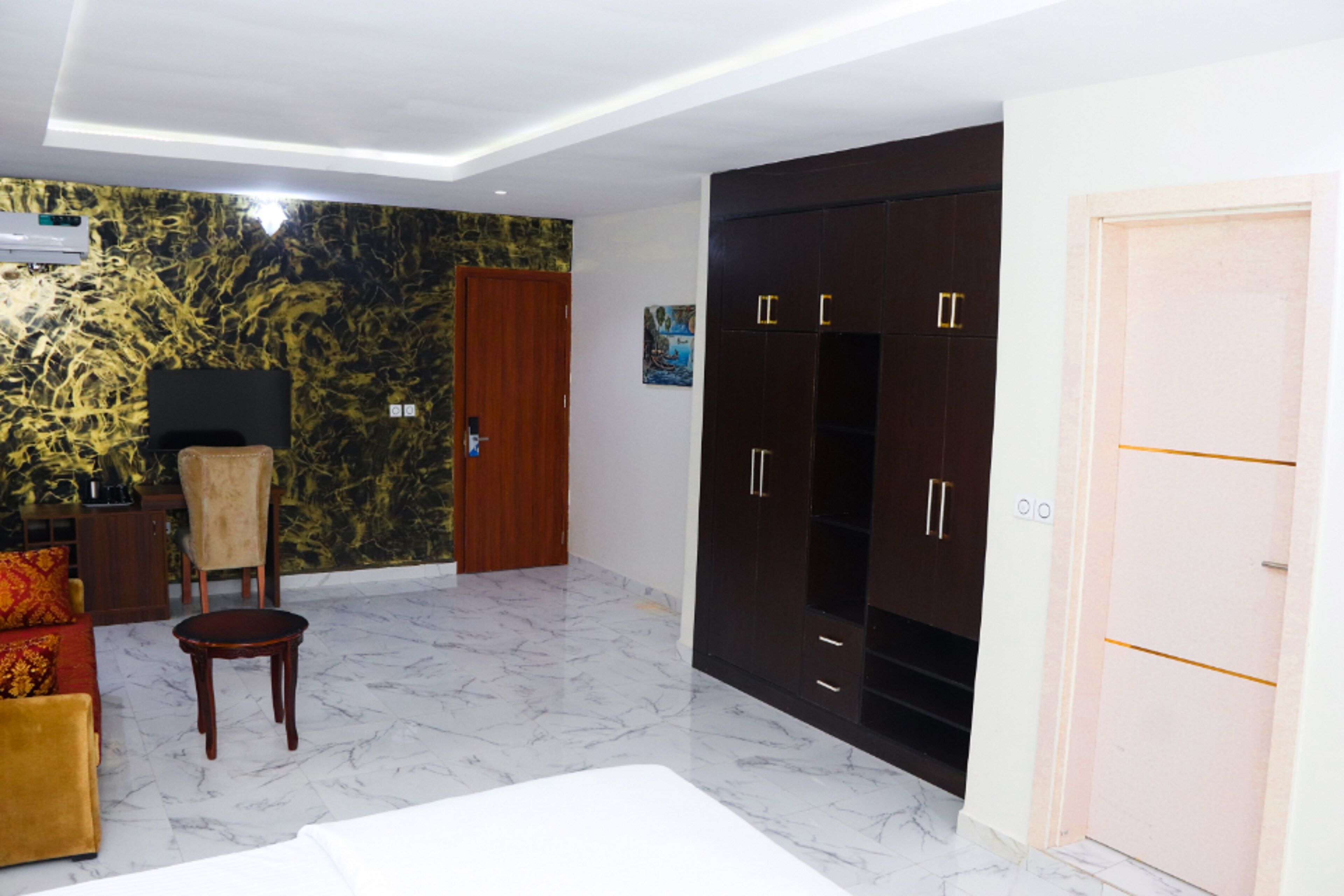 A spacious room with a large wardrobe, a wooden chair, a small table, and a sofa.