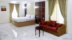 A hotel room with a bed, a sofa, a small table, and curtains. - Ibom Waterfall Resorts and Suites (Arochukwu)